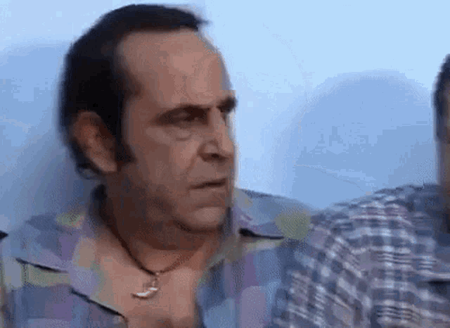 a man wearing a plaid shirt and a necklace is looking at something .