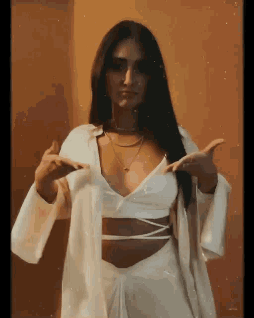 a woman wearing a white crop top and a white jacket is standing in front of a wall .