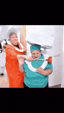a woman in a green shirt is holding a plunger over a man in an orange shirt