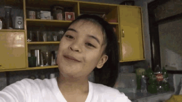 a girl taking a selfie in a kitchen with a bottle of coca-cola in the background