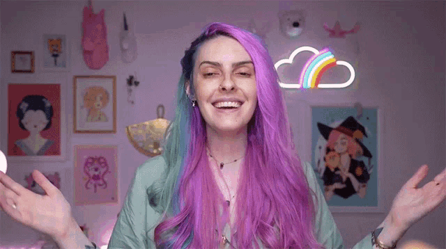 a woman with purple hair is smiling with her arms outstretched in front of a rainbow sign