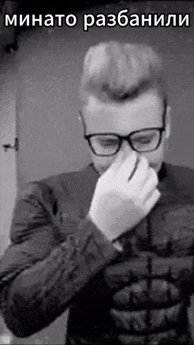 a man wearing glasses and a jacket is covering his nose with his hand .