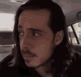 a man with long hair and a mustache is sitting in the back of a car .