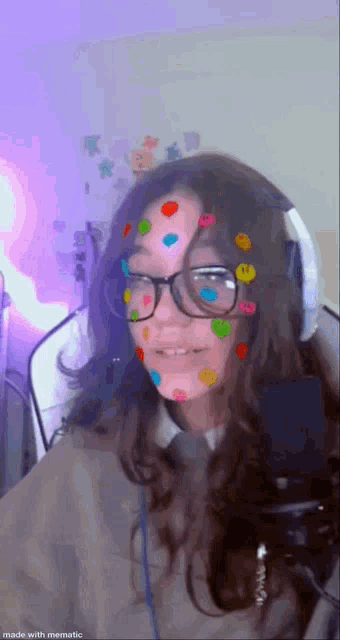 a girl with glasses and smiley faces on her face is standing in front of a microphone .