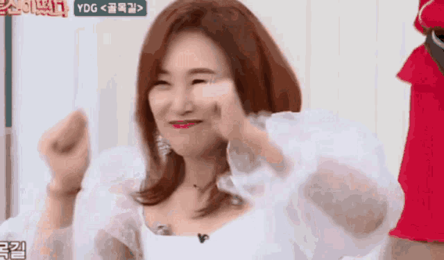 a woman with red hair is making a funny face with her hands in the air in front of a sign that says ydg