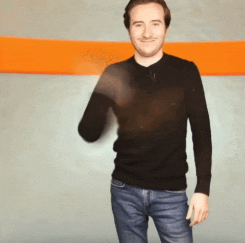 a man in a black sweater and blue jeans is standing in front of an orange and grey wall