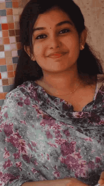 a woman wearing a purple and green floral shirt smiles for the camera