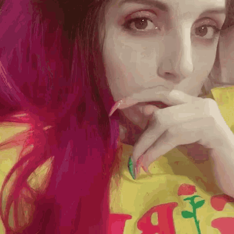 a woman with pink hair is wearing a yellow shirt with a flower on it .