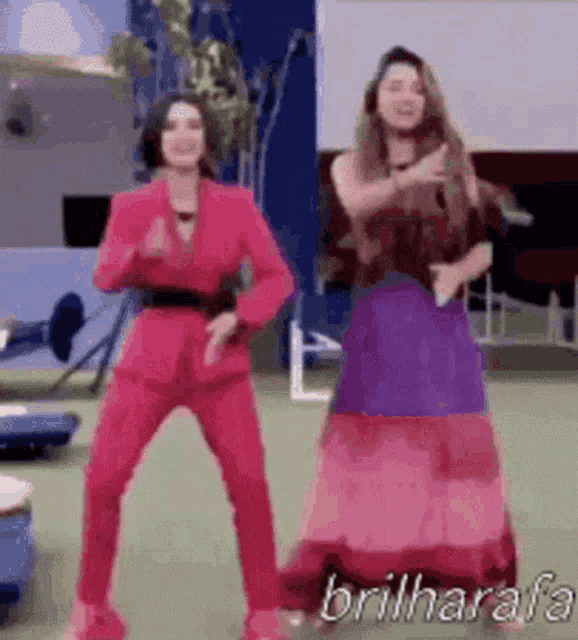 two women in pink suits and purple dresses are dancing together on a green field .