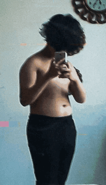 a woman taking a picture of herself in a mirror with a clock in the background