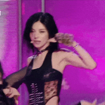 a woman in a black top is dancing on a stage with a purple background .