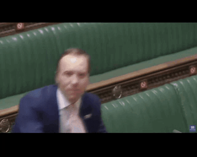 a blurry picture of a man in a suit sitting in a parliament .