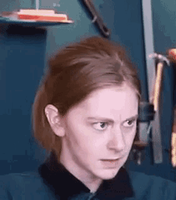 a woman in a blue shirt is making a funny face in front of a wall with hammers hanging on it .