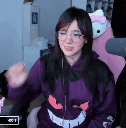 a girl wearing glasses and a purple hoodie is sitting in front of a pink hello kitty pillow