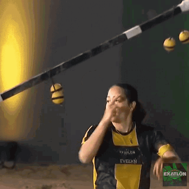 a woman is juggling balls in front of a green exatlon sign