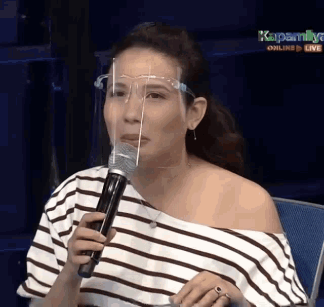 a woman wearing a face shield is holding a microphone in front of her face .