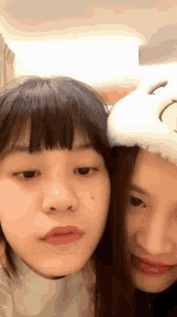 two girls are making funny faces with one wearing a hat that has a smiley face on it