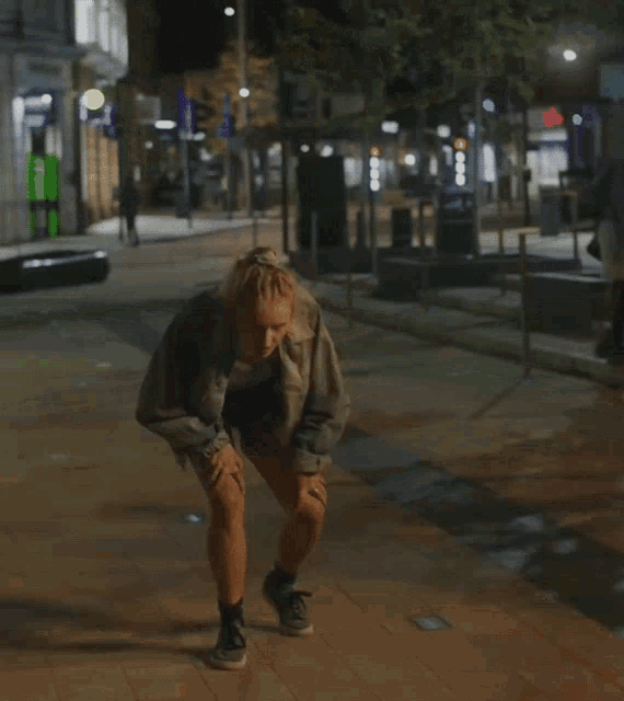 a man kneeling down on a sidewalk with his hands on his knees in front of a store that has a green sign on it