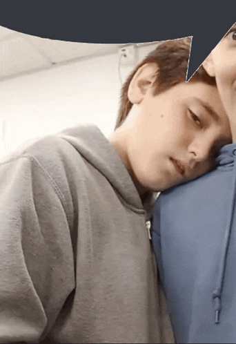 a boy in a grey hoodie leans his head on another boy 's shoulder