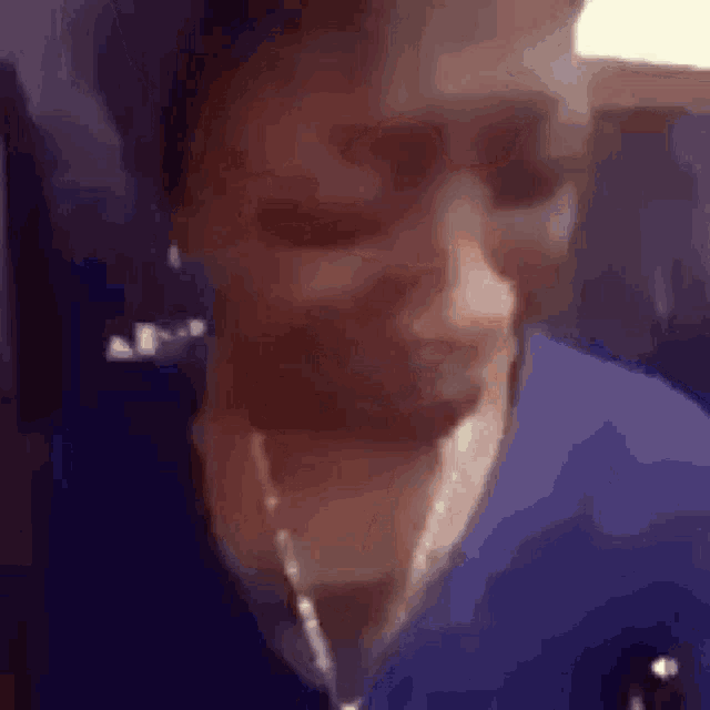 a close up of a woman 's face wearing a blue shirt and a chain around her neck .