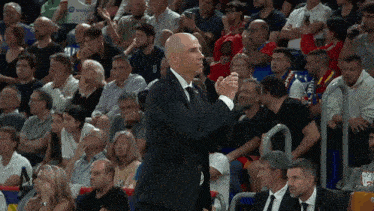 a man in a suit applauds in front of a crowd with a jersey that says u