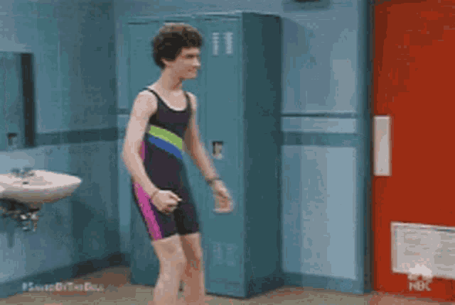 a man in a bathing suit is standing in front of a locker .