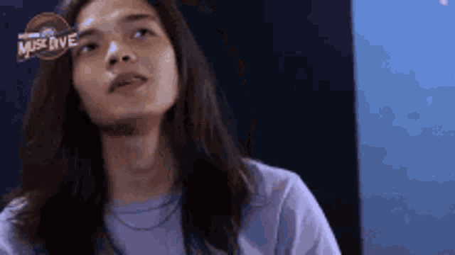 a woman with long hair is wearing a purple shirt and looking up at something .