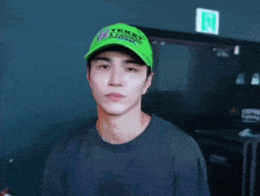 a young man wearing a green teket hat is making a peace sign