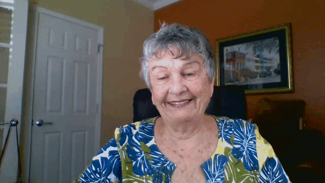 an elderly woman in a blue and yellow shirt smiles in front of a door