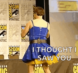 a woman in a blue dress is standing in front of a comic con sign .