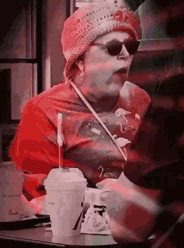 a woman wearing sunglasses and a red hat is sitting at a table with a cup that says chick-fil-a on it