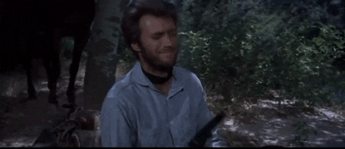 a man with a beard is holding a gun in a forest .