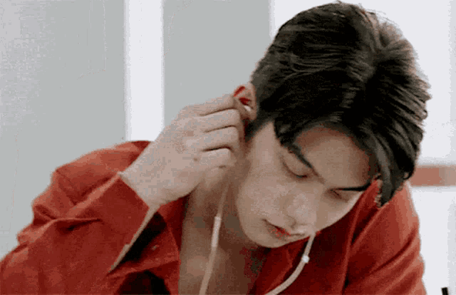 a young man in a red shirt is putting on ear buds .