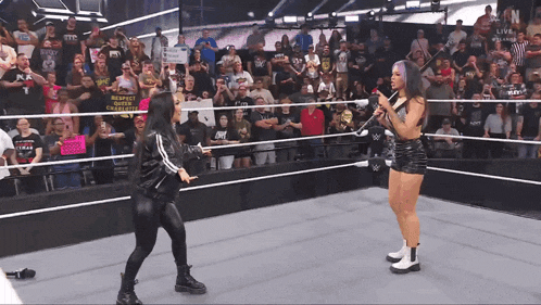 two women in a wrestling ring with one holding a microphone and a sign that says respect the crazy