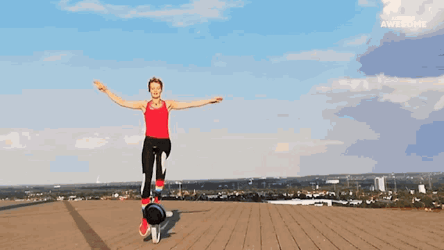 a woman in a red tank top is balancing on a skateboard on a rooftop with the word awesome on the bottom