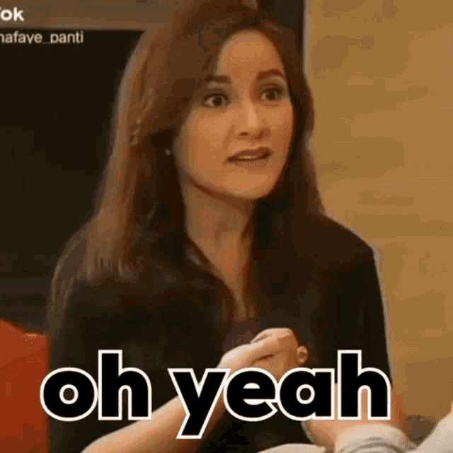a woman is sitting on a couch talking to someone and the words oh yeah are on the screen .