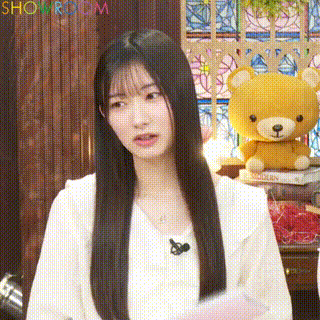 a woman with long hair is standing in front of a teddy bear and a stained glass window .