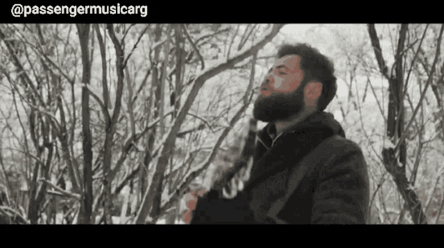 a man with a beard is standing in the snow with passengermusicarg written on the bottom