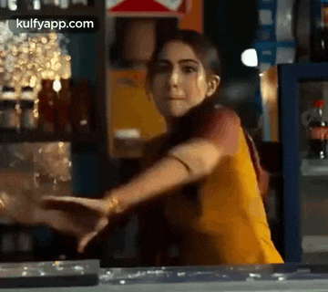 a woman in a yellow dress is standing at a counter in front of a coca cola refrigerator .