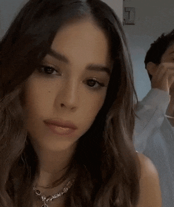 a woman is applying lip gloss to her lips while a man looks on .