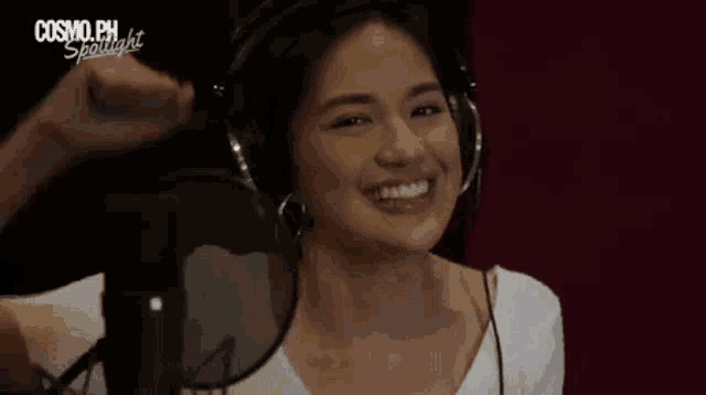 a woman wearing headphones is smiling in front of a microphone in a studio .