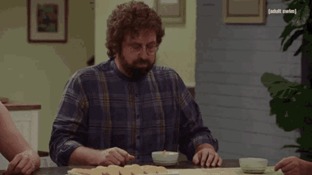 a man in a plaid shirt is sitting at a table with a bowl of food and a sign that says adult swim on it