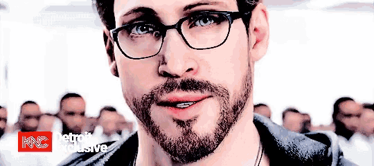 a man with glasses and a beard is smiling in front of a crowd and the words detroit exclusive are visible