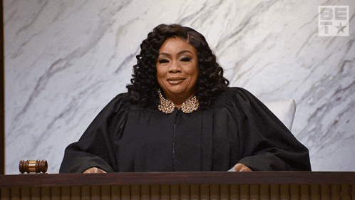 a woman in a judge 's robe sits at a desk in front of a sign that says be free