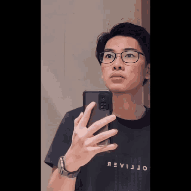 a man wearing glasses takes a selfie in front of a mirror with his phone