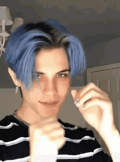 a young man with blue hair is wearing a black and white striped shirt and making a funny face .