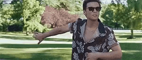 a man wearing sunglasses and a shirt is standing in a park .