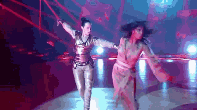 two women are dancing on a stage in a dark room with red lights .