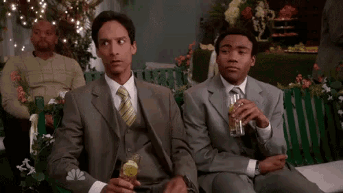 two men in suits and ties are sitting on a bench drinking a drink .