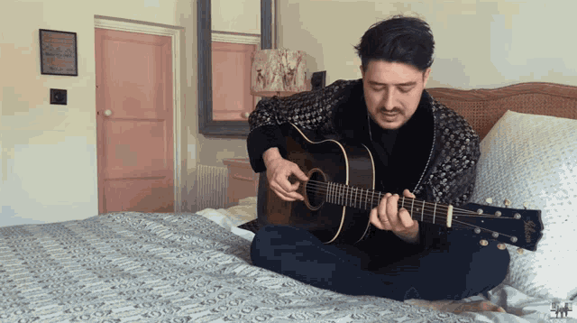 a man is sitting on a bed playing a guitar with a sign on the wall that says ' i love you '